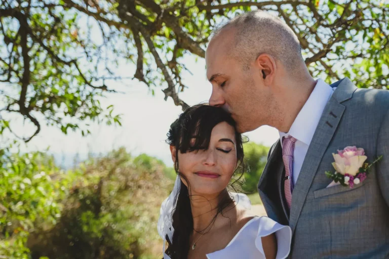 un marié qui embrasse sa compagne sur le front dans un parc lors de la séance couple de leur mariage