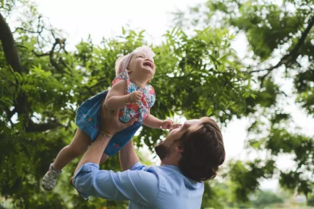 photo de famille d'un papa soulevant sa petite fille en l'air dans une roseraie