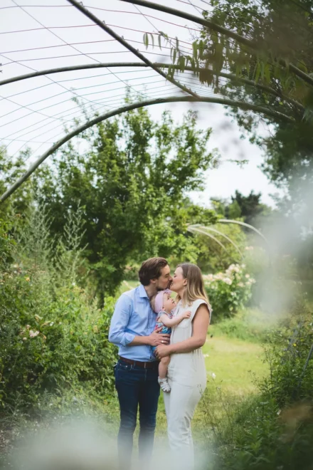 photo de famille avec deux parents se faisant un bisou et tenant leur bébé dans les bras