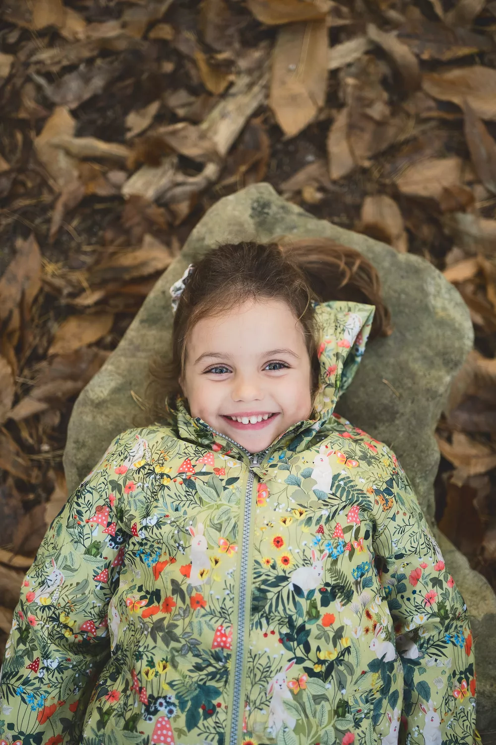 portrait de famille d'une petite fille de face allongée sur un caillou et souriant