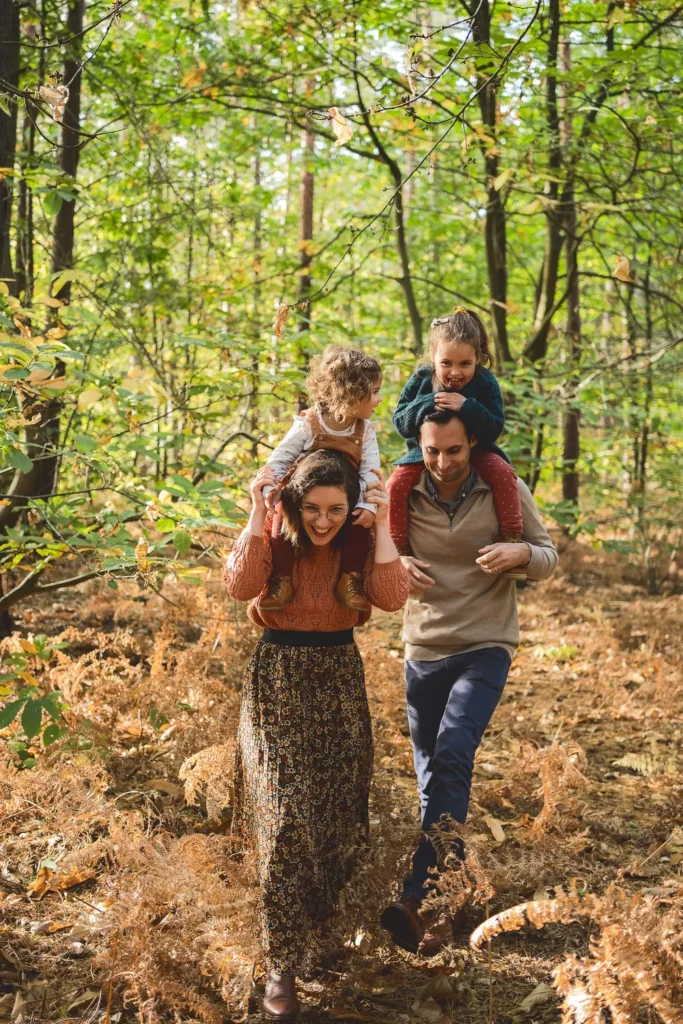 photo de famille de deux parents et leurs deux enfants sur les épaules dans la forêt