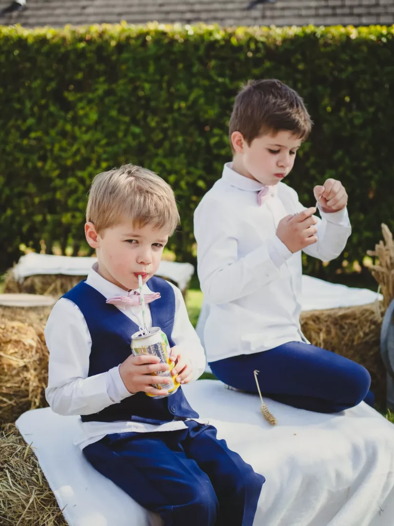 deux jeunes enfants en train de boire et manger sur des ballots de paille lors du vin d'honneur du mariage de leurs parents en ile de france